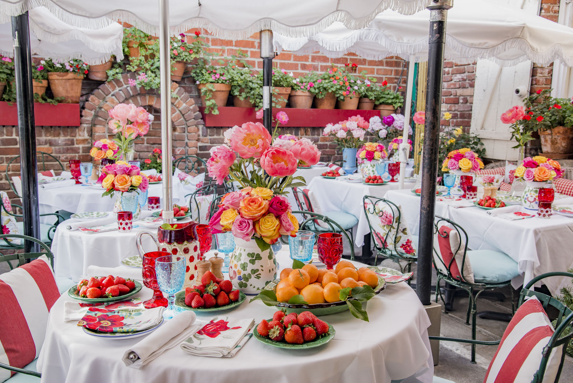 The Ivy Restaurant outdoor patio with french garden chairs, roses and peonies on every 
									table, plates of strawberries and a pitcher of fresh lemonade, pots of geraniums on the 
									wall and umbrellas overhead.