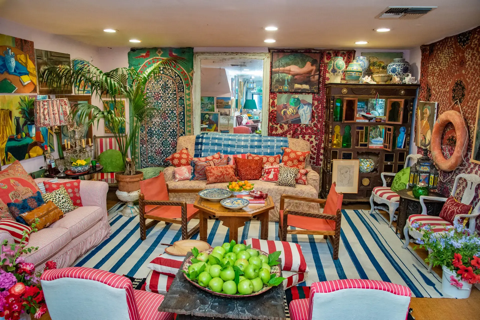 Inside the Indigo Seas boutique — striped rugs, rose-print sofas, folk art, ceramics, and a bowl of green apples on a carved table